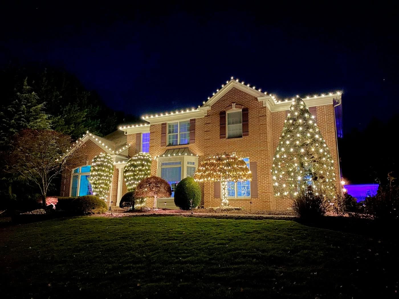 Two story home with warm white roofline and tree lights