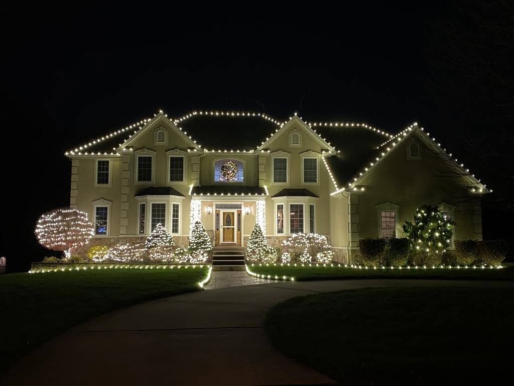 Two story home with white roofline, window and garden Christmas lights at night