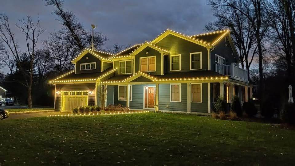 Two story home with warm white roofline lights at dusk